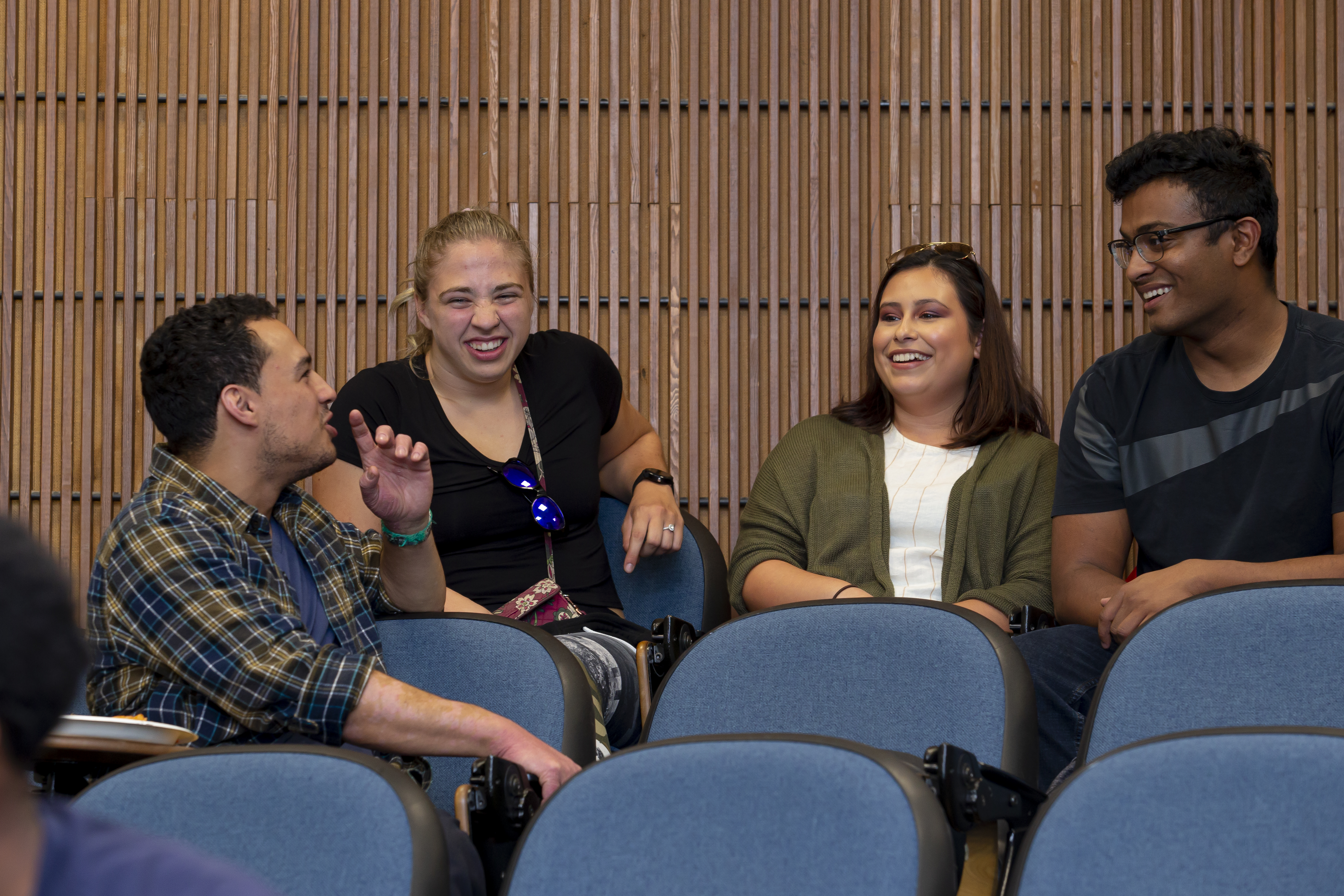 four students talking and laughing at the back of an auditorium classroom